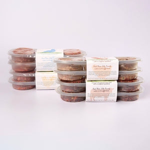 Four stacked plastic containers filled with LUNA & me Everyday Box raw dog food patties
